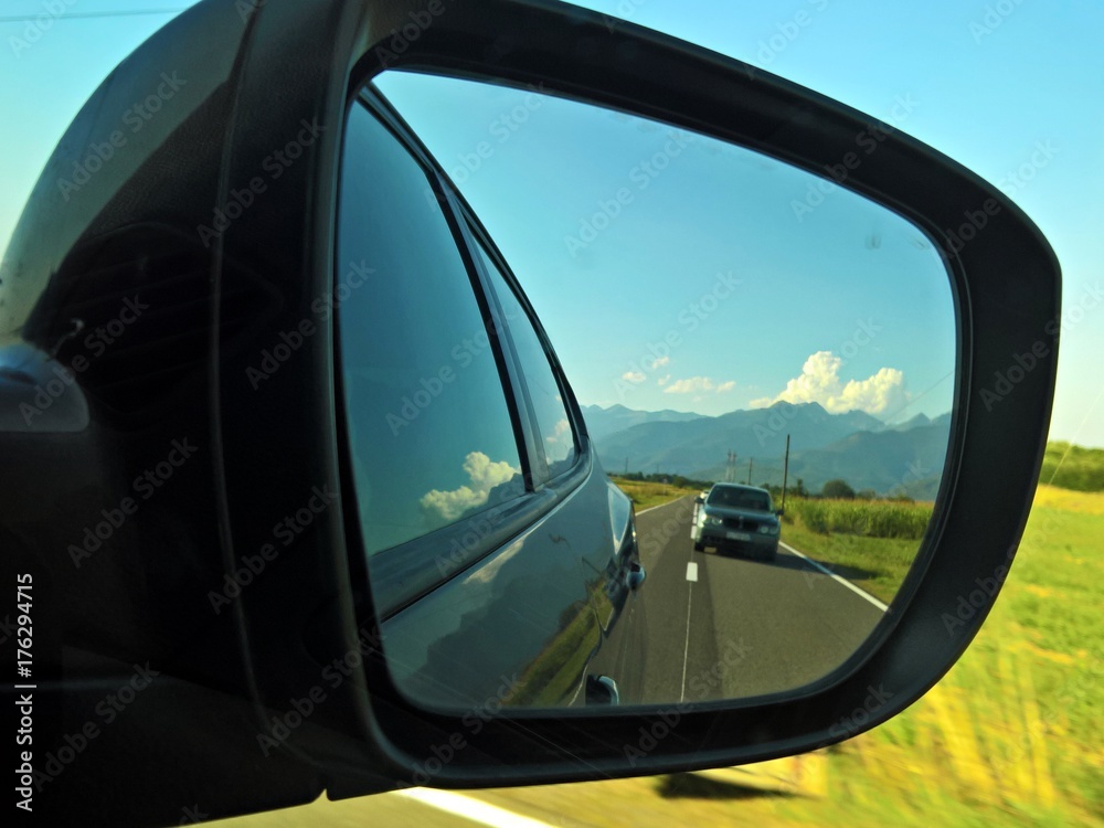 Rear view mirror reflecting road and sky in a beautiful summer day