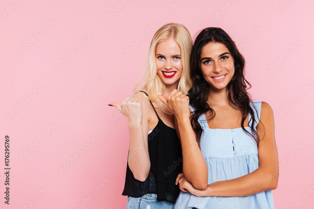 Two smiling women pointing away and looking at the camera