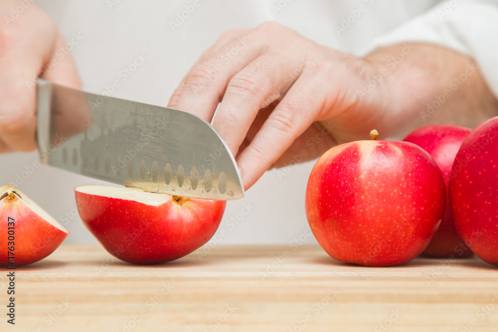 Φωτογραφία Chef's hands with knife cutting the red apples on the wooden board for pie, cake, sweet dessert or snack in the kitchen