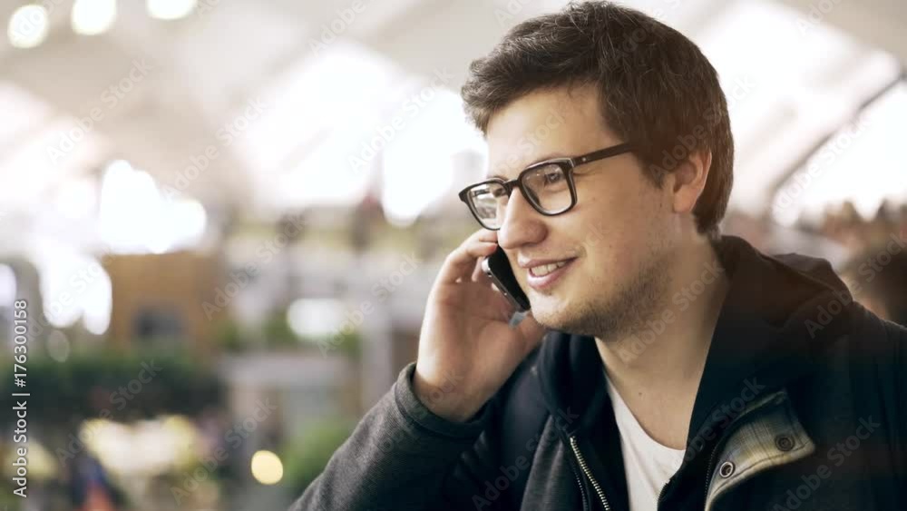 Attractive young man drinking a coffee to go and having a phone conversation while shopping at a farmer s market. Handheld real time medium shot