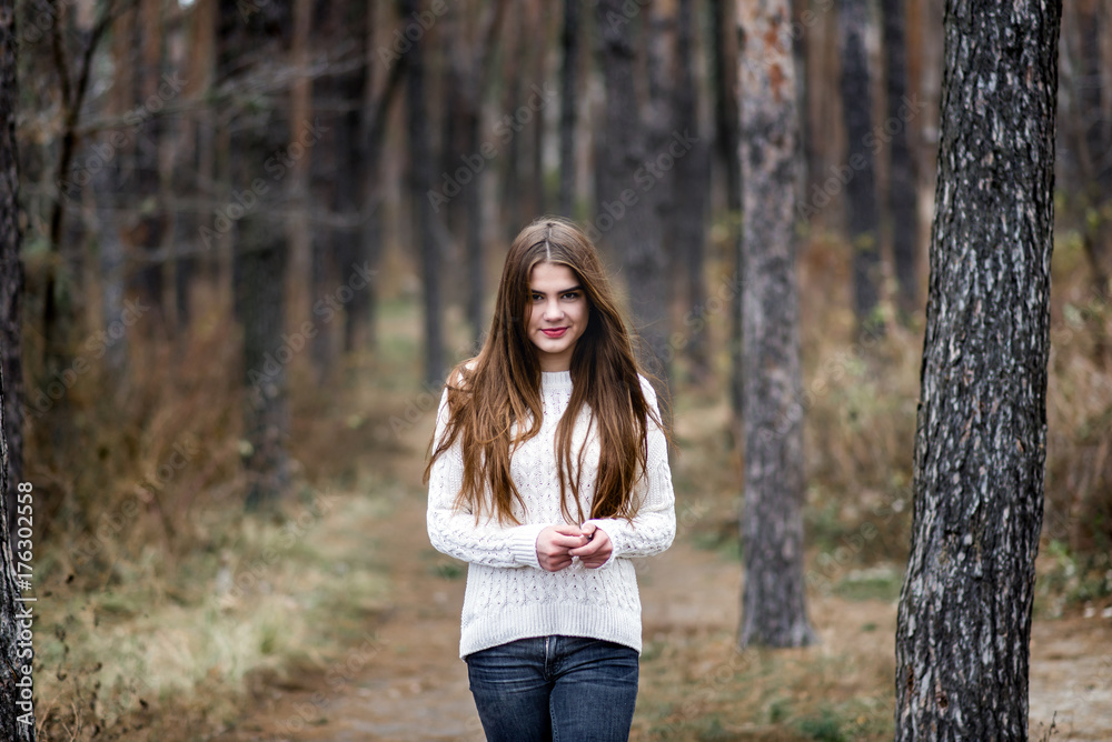 Portrait of a beautiful girl standing in an autumn forest and dressed in a white warm sweater Portrait of a beautiful girl standing in an autumn forest and dressed in a white warm sweater