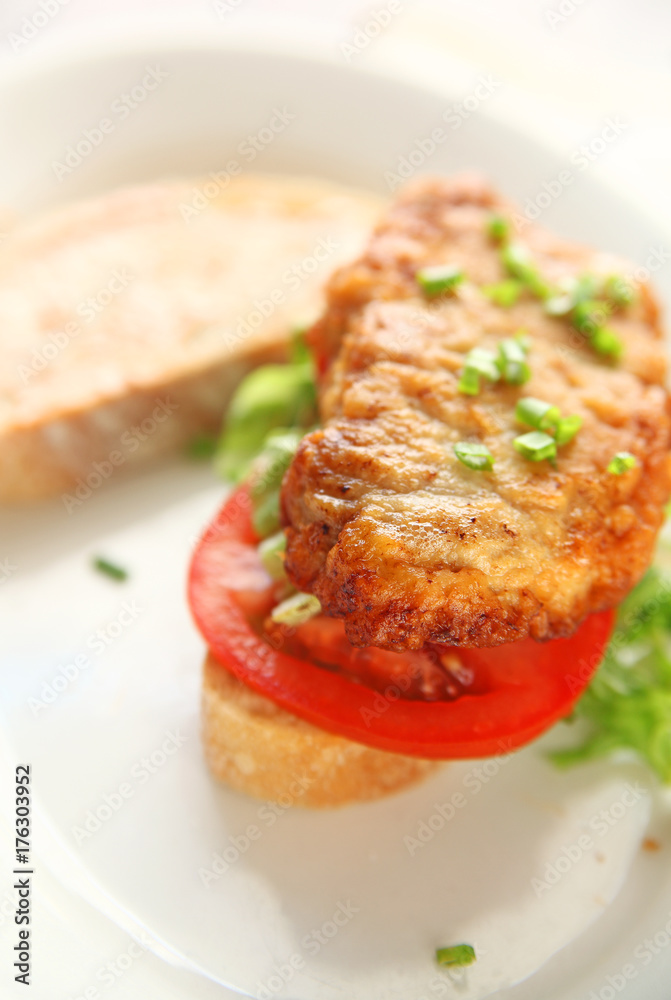 A battered and fried pork cutlet with tomato, chopped lettuce and scallions on artisan bread