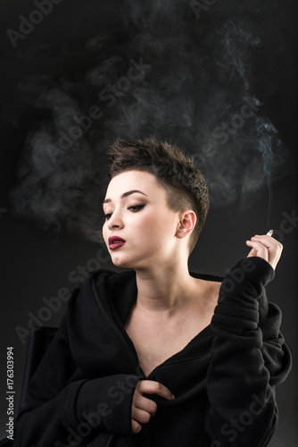 Young beautiful girl sitting in chair and smoking against the dark background © speed300