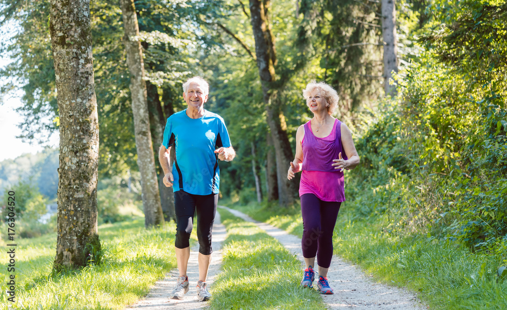 Full length front view of two active seniors with a healthy lifestyle smiling while jogging together outdoors in the park