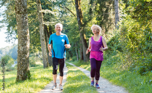 Full length front view of two active seniors with a healthy lifestyle smiling while jogging together outdoors in the park