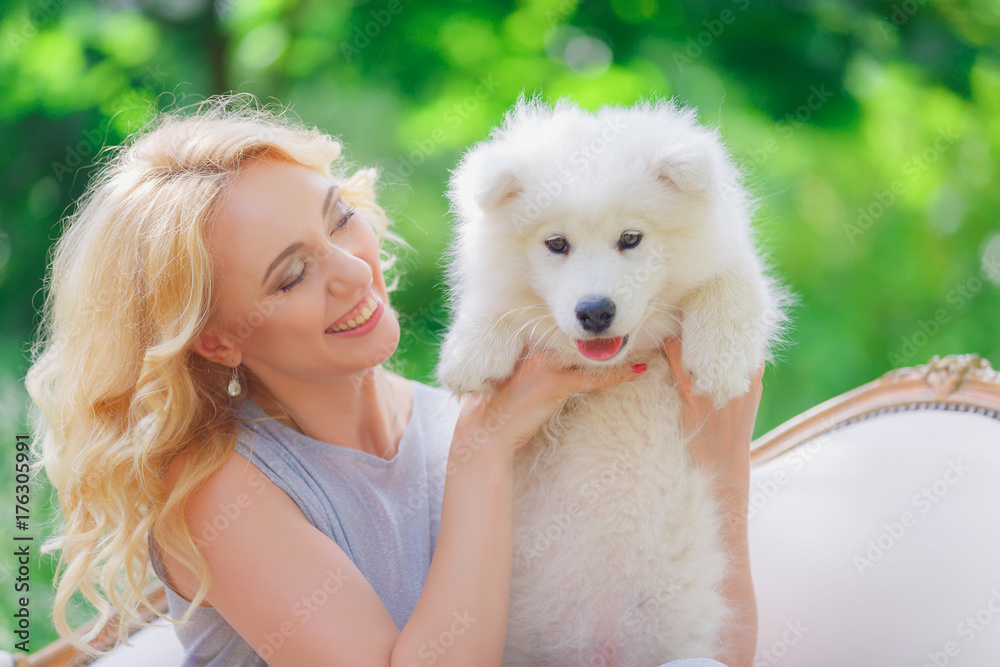 Beautiful young girl with a white puppy in her arms on a retro sofa in a summer garden Beautiful young girl with a white puppy in her arms on a retro sofa in a summer garden