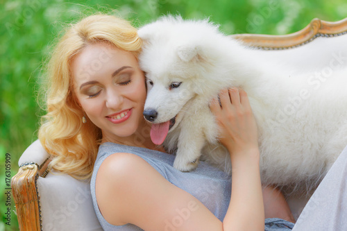 Beautiful young girl with a white puppy in her arms on a retro sofa in a summer garden © viktoriia1974