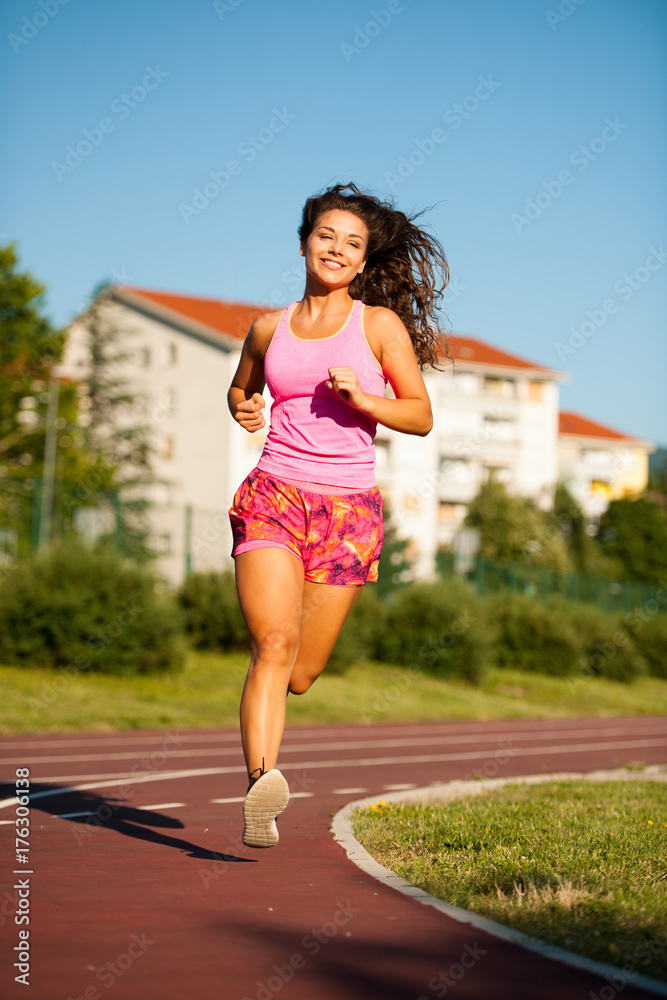 active young woman runs on atheltic track on summer afternoon
