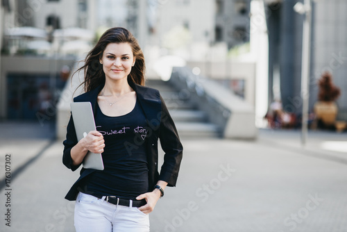 Business woman with a laptop standing on a street in a modern city