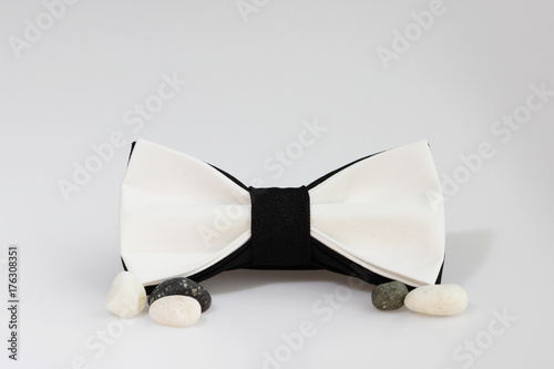 Composition: Extravagant black and white bow tie and sea pebbles on a white background photo