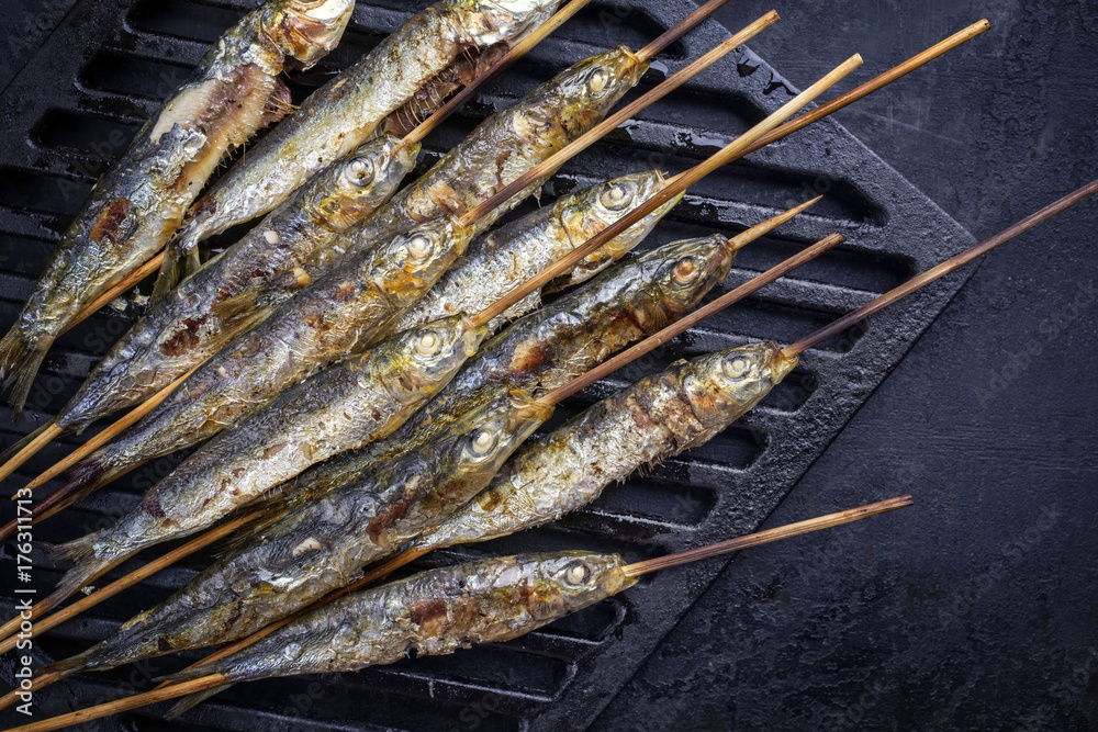 Traditional Spanish barbecue sardines on a wooden skewer as top view on a grillage Traditional Spanish barbecue sardines on a wooden skewer as top view on a grillage