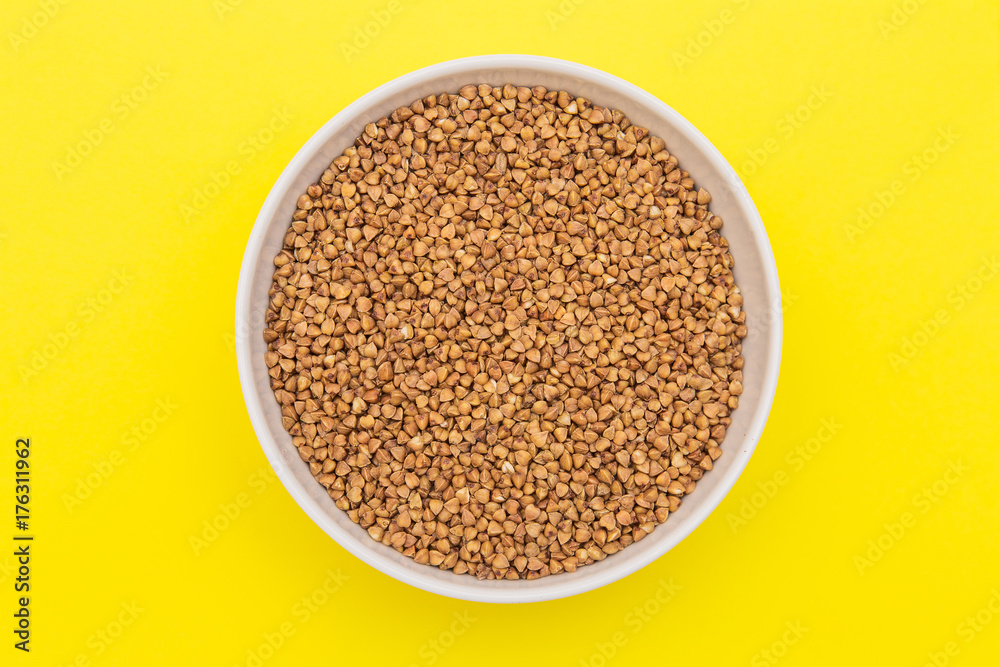 A buckwheat in round white plate on yellow background, a bunch of buckwheat grain in white plate A buckwheat in round white plate on yellow background, a bunch of buckwheat grain in white plate