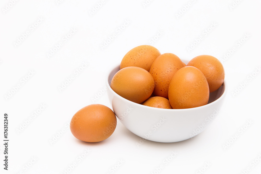 Raw brown eggs in a white plate on a white background, egg near the plate Raw brown eggs in a white plate on a white background, egg near the plate