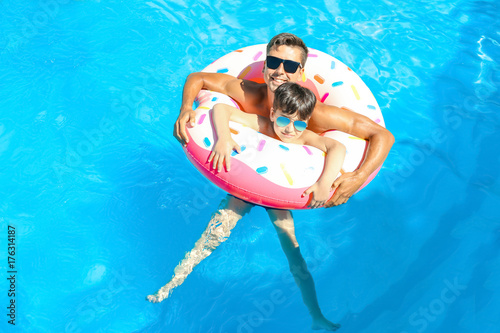 Young man and his son with inflatable donut in swimming pool