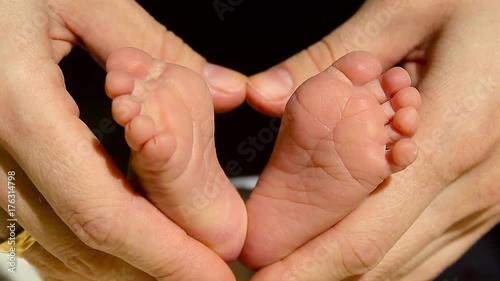 Baby feet in mother hands. Tiny Newborn Baby's feet on female Heart Shaped hands closeup. Mom and her Child. Happy Family concept. Beautiful conceptual video of Maternity. photo