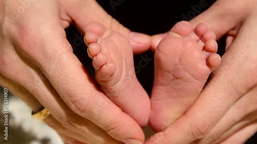 Baby feet in mother hands. Tiny Newborn Baby's feet on female Heart Shaped hands closeup. Mom and her Child. Happy Family concept. Beautiful conceptual video of Maternity. photo