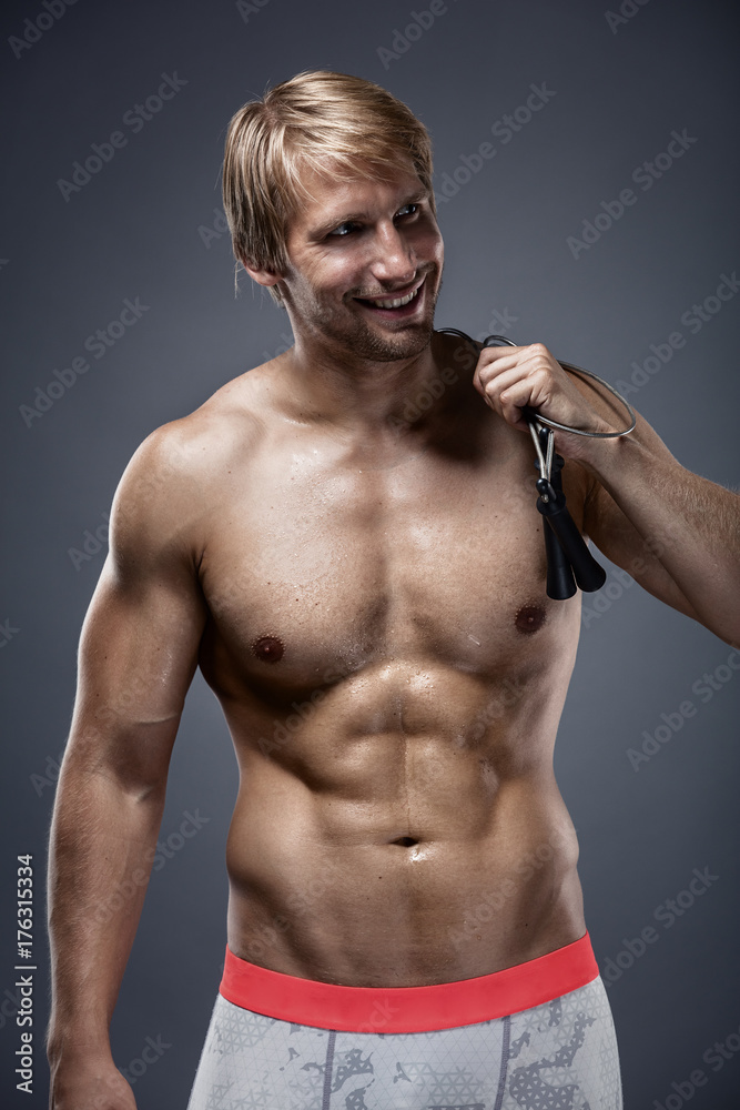 Obraz premium Muscular bodybuilder guy doing exercises with jump rope