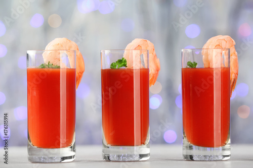 Glasses of tomato sauce and shrimps on table against sparkly background, closeup