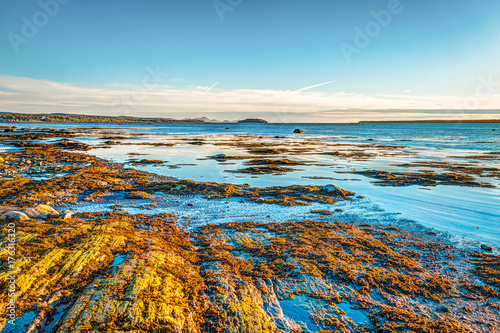 Sunset in Rimouski, Quebec by Saint Lawrence river in Gaspesie region of Canada with rock boulders in shallow blue turquoise water photo