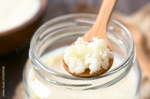 Milk kefir grains on wooden spoon on top of a jar of kefir, photographed with natural light (Selective Focus, Focus in the middle of the kefir grains) photo