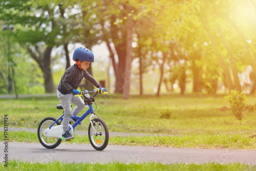 Happy kid boy of 5 years having fun in spring park with a bicycle on beautiful fall day. Active child wearing bike helmet