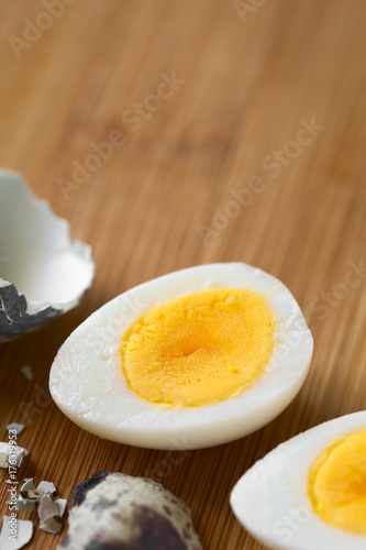 Hard boiled quail egg halves with egg shells on wooden board, photographed with natural light (Selective Focus, Focus in the middle of the egg half)