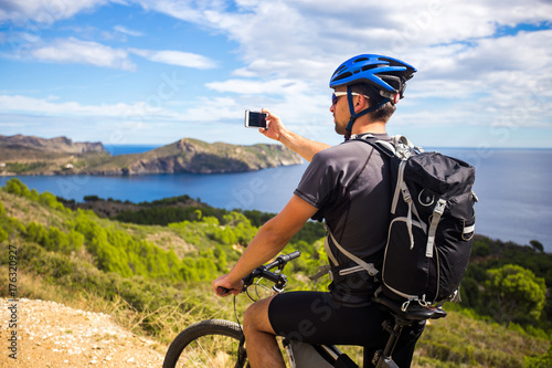 Foto a young guy on a mountain bike trails in Spain and takes a photo on a white phone in the background of the Mediterranean sea of the rocky coast of the Costa Brava