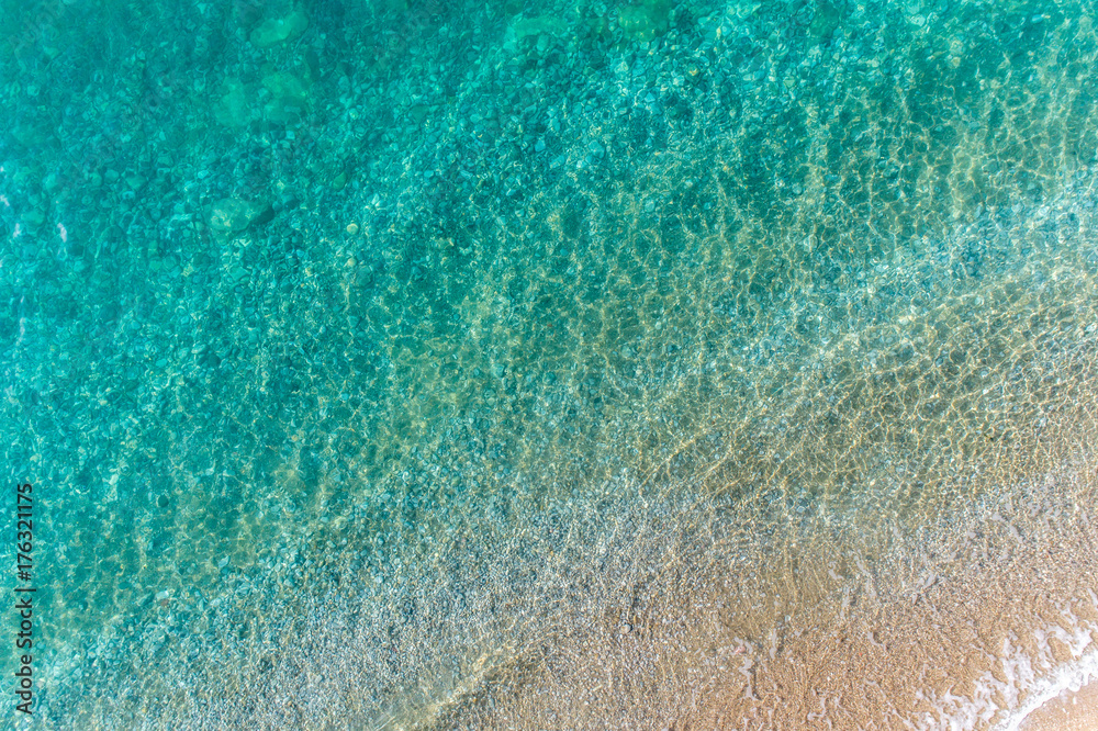 Waves of turquoise color roll on the sandy beach aerial view