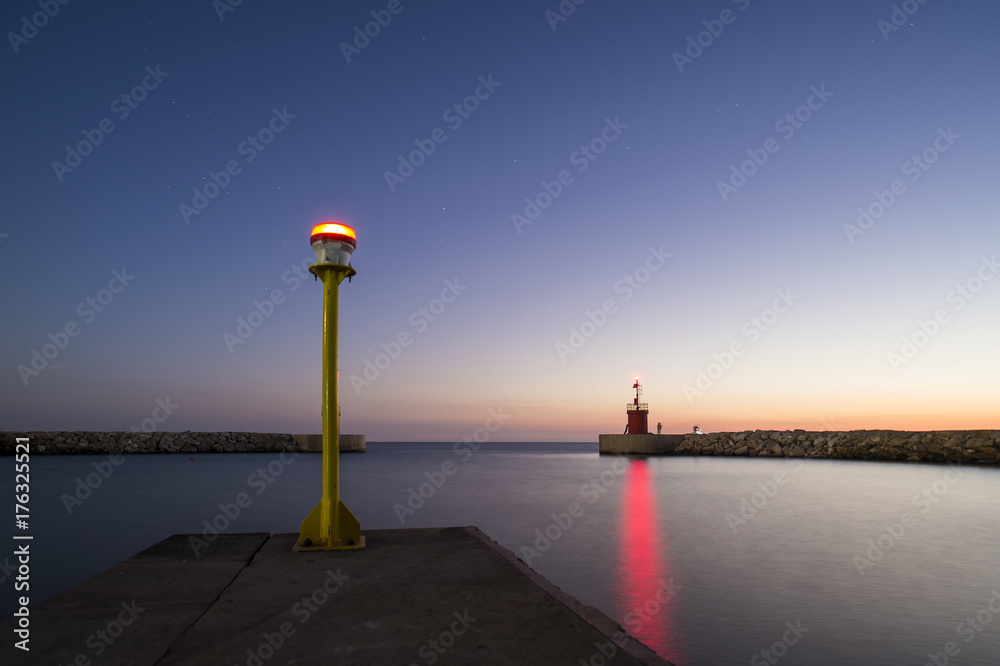 Seascape of a small lighthouse with his red reflections on the sea at sunset. Some people are fishing under the starry sky. Photo taken at sunset in Sabaudia beach, Italy