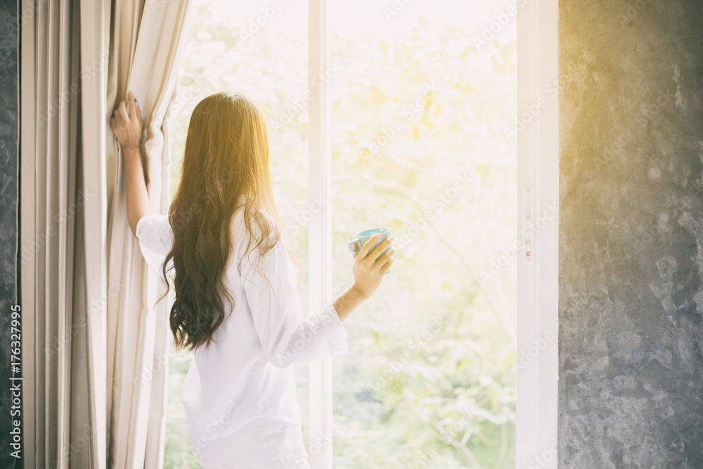 Asian women drinking coffee and wake up in her bed fully rested and open the curtains in the morning to get fresh air on sunshine Asian women drinking coffee and wake up in her bed fully rested and open the curtains in the morning to get fresh air on sunshine