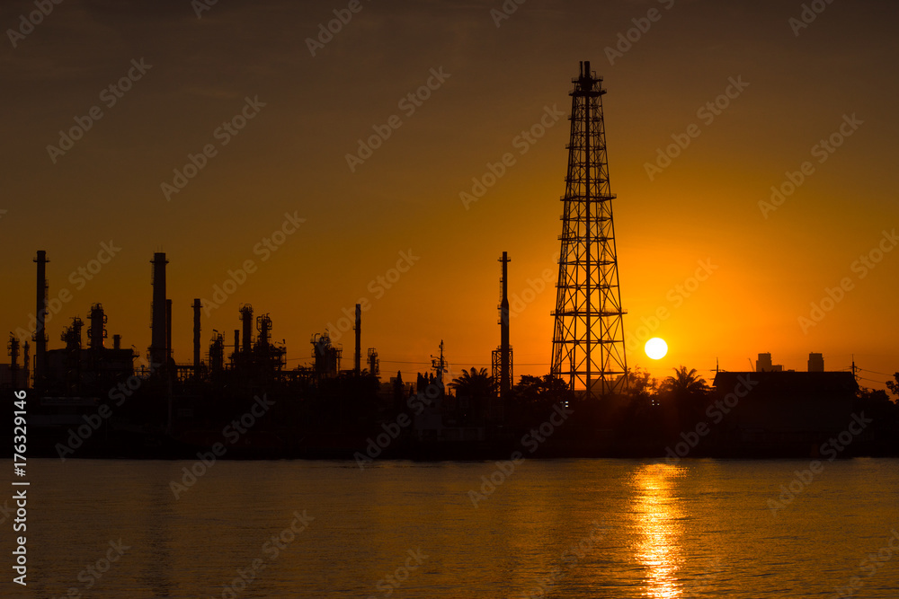 Silhouette oil refinery and petrochemical plant at sunrise time beside Chao Phaya river, Thailand. Light reflection on the smooth water.