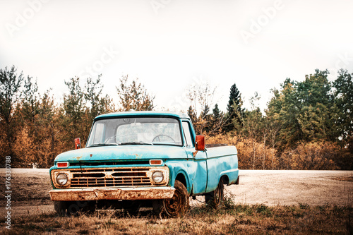 A vintage two door green truck parked on the road side in front of autumn trees