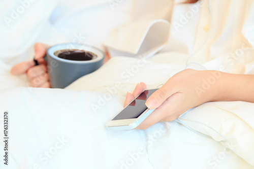young woman drinking coffee in her bedroom and checking her smaitphone in the morning