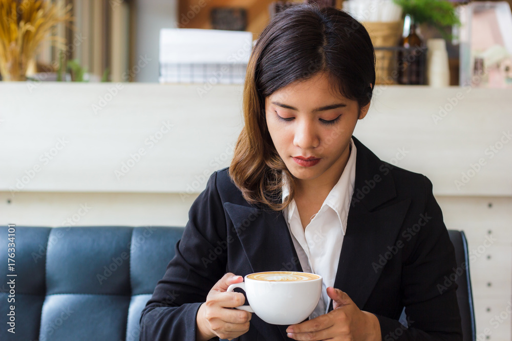 A beautiful asian business woman sitting on sofa and looking cup of hot coffee in her hand. Business woman relaxing in coffee shop. Copy space. A beautiful asian business woman sitting on sofa and looking cup of hot coffee in her hand. Business woman relaxing in coffee shop. Copy space.