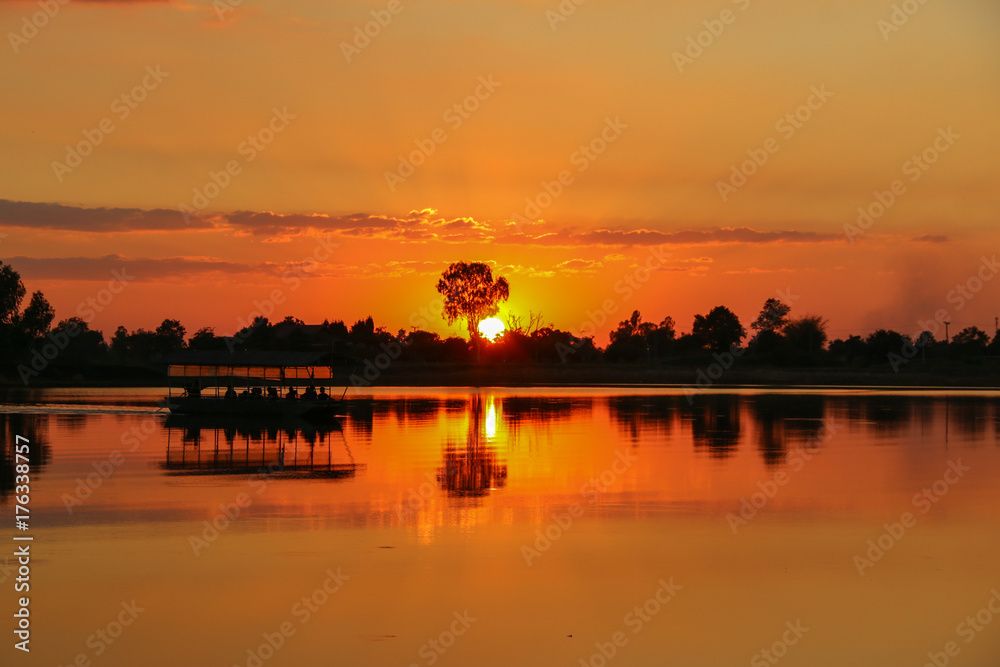 Silhouette photo of people exploring on the boat in the evening with Sunset over the lake and the  reflection.Orange sky background.