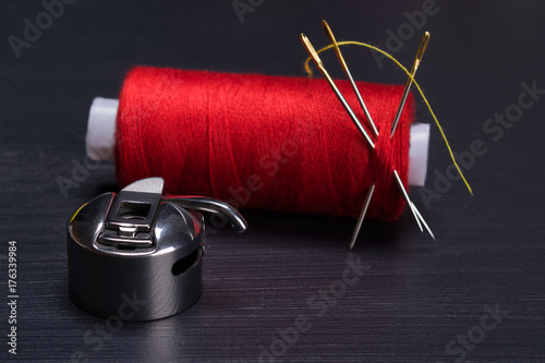 red skein of thread at the needle and the Shuttle hook for sewing machine, on a dark background