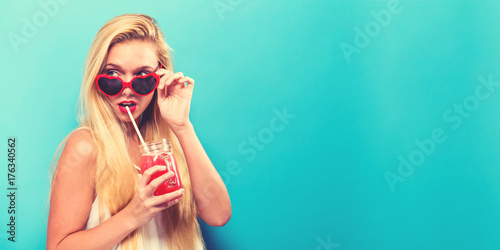 Happy young woman drinking smoothie on a solid background