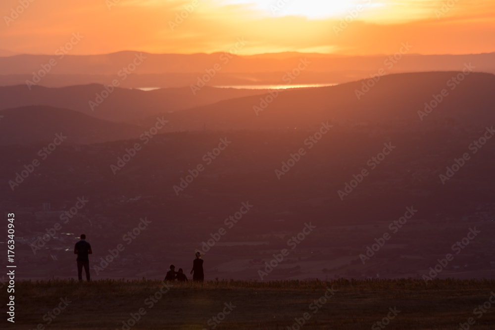A family on a mountain peak looking over a valley at sunset
