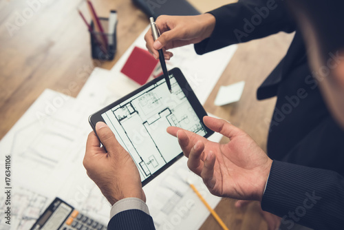 Real estate agent with client or architect team checking a housing model and its blueprints digitally using a tablet