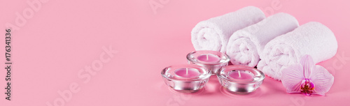 Towels, candles and orchid flowers for a spa relaxation on a pink background.