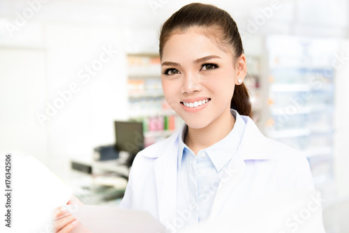 Smiling young Asian woman pharmacist working in pharmacy (or drugstore)