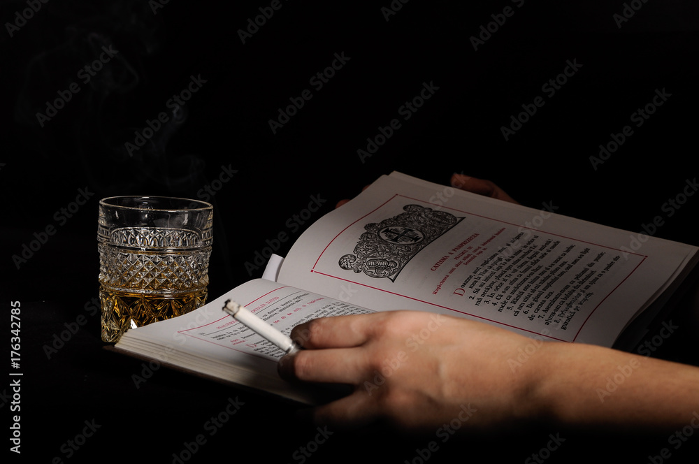 Naklejka premium Woman hands smoking and drinking - Close up of adult woman hands holding a cigarette near a glass of alcohol and reading a Bible