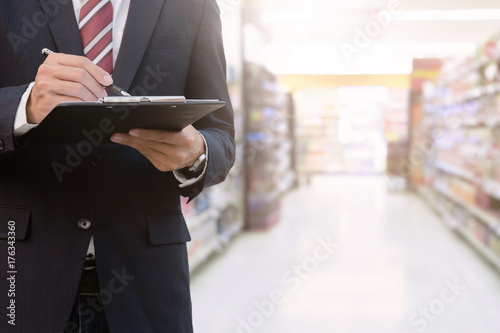 business man working on clipboard standing in front of supermarket background