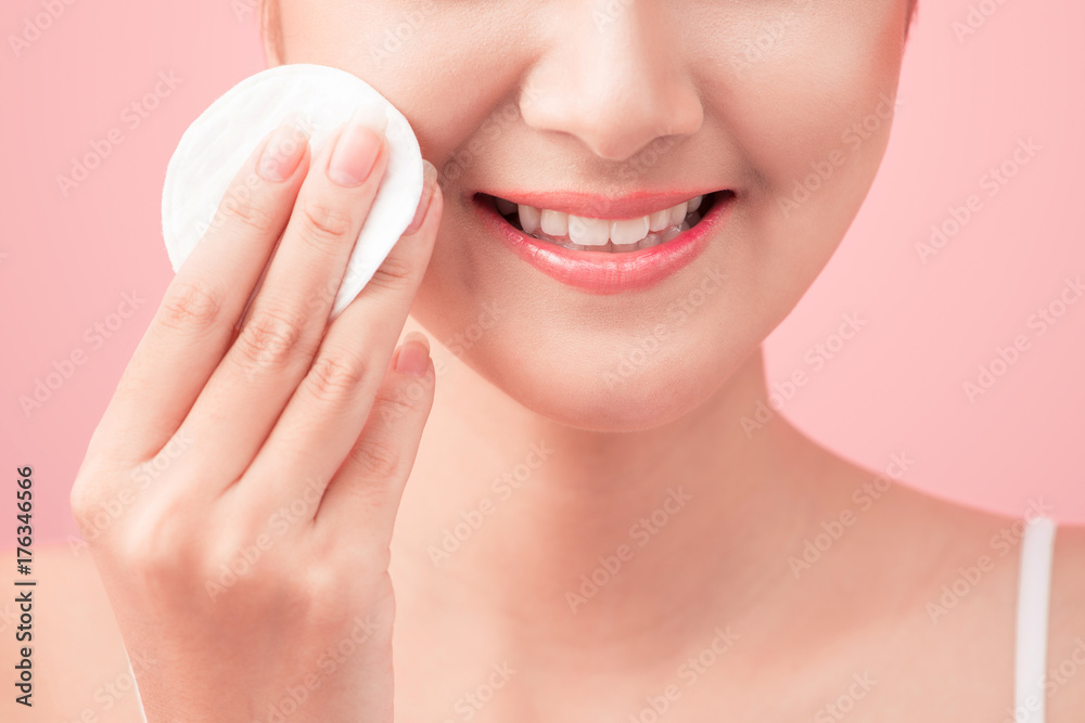 Gorgeous young woman holding cotton pad and smiling in taking care of her face for fresh healthy skincare on pink background Gorgeous young woman holding cotton pad and smiling in taking care of her face for fresh healthy skincare on pink background