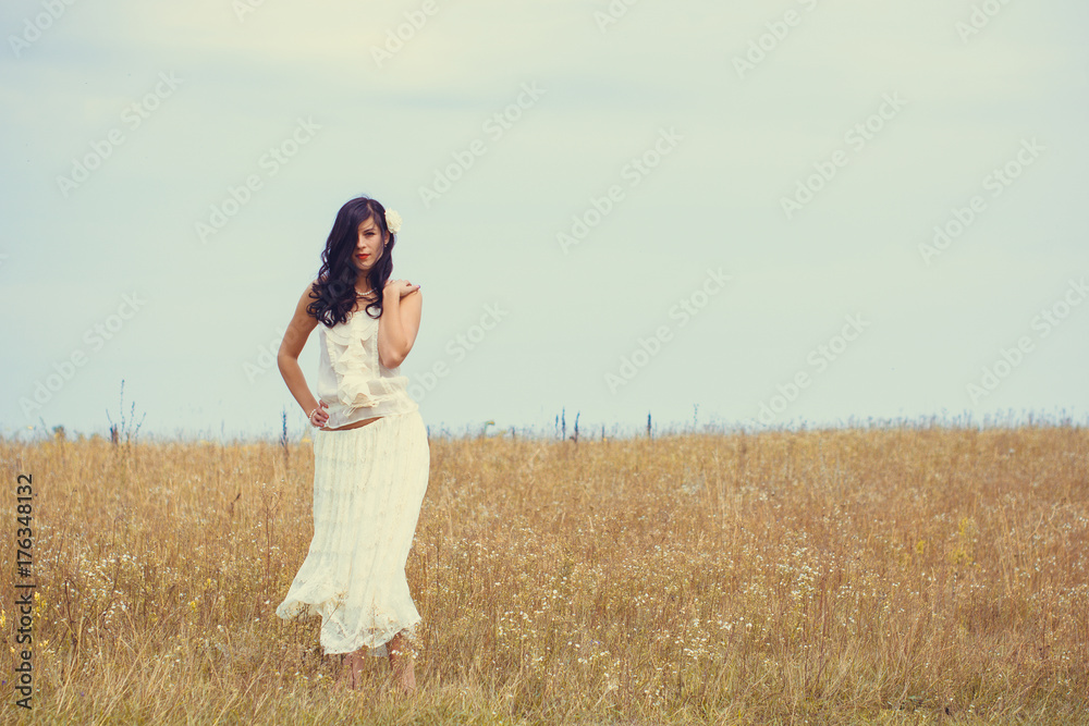 Beautiful curly and tanned woman in lace vintage blouse and skirt on a meadow. Concept of retro femininity and tenderness