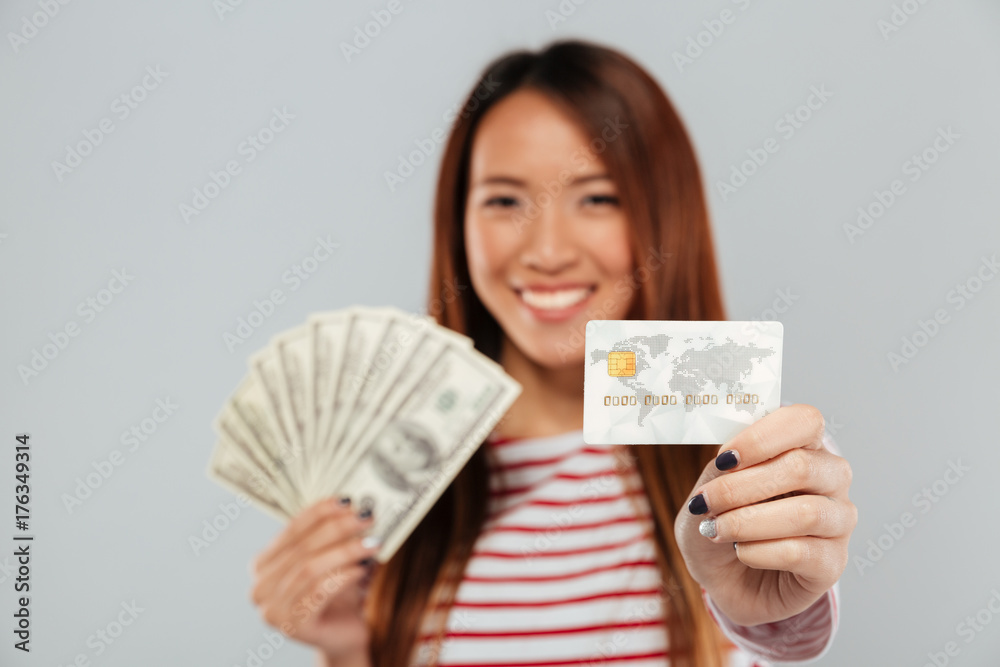 Asian lady over grey wall holding money and credit card. Asian lady over grey wall holding money and credit card.