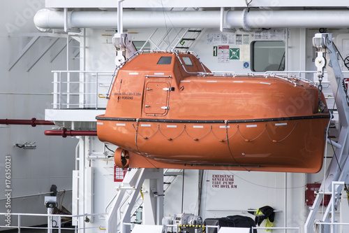 Orange inclosed lifeboat hung from davits an a ship