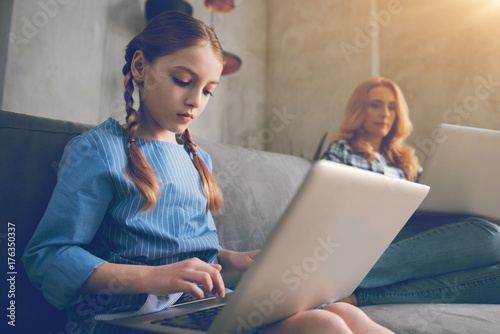 Serious young girl typing on laptop next to mother