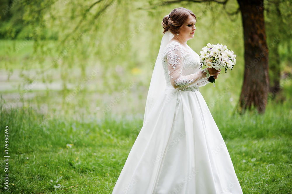 Portrait of a beautiful young bride posing with a bouquet outdoor on her own.