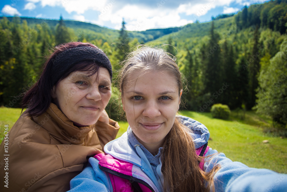 Mom and adult daughter sitting on the top of mountains and taking selfie. Happy senior women and daughter taking selfie together. Holiday daughter with mother